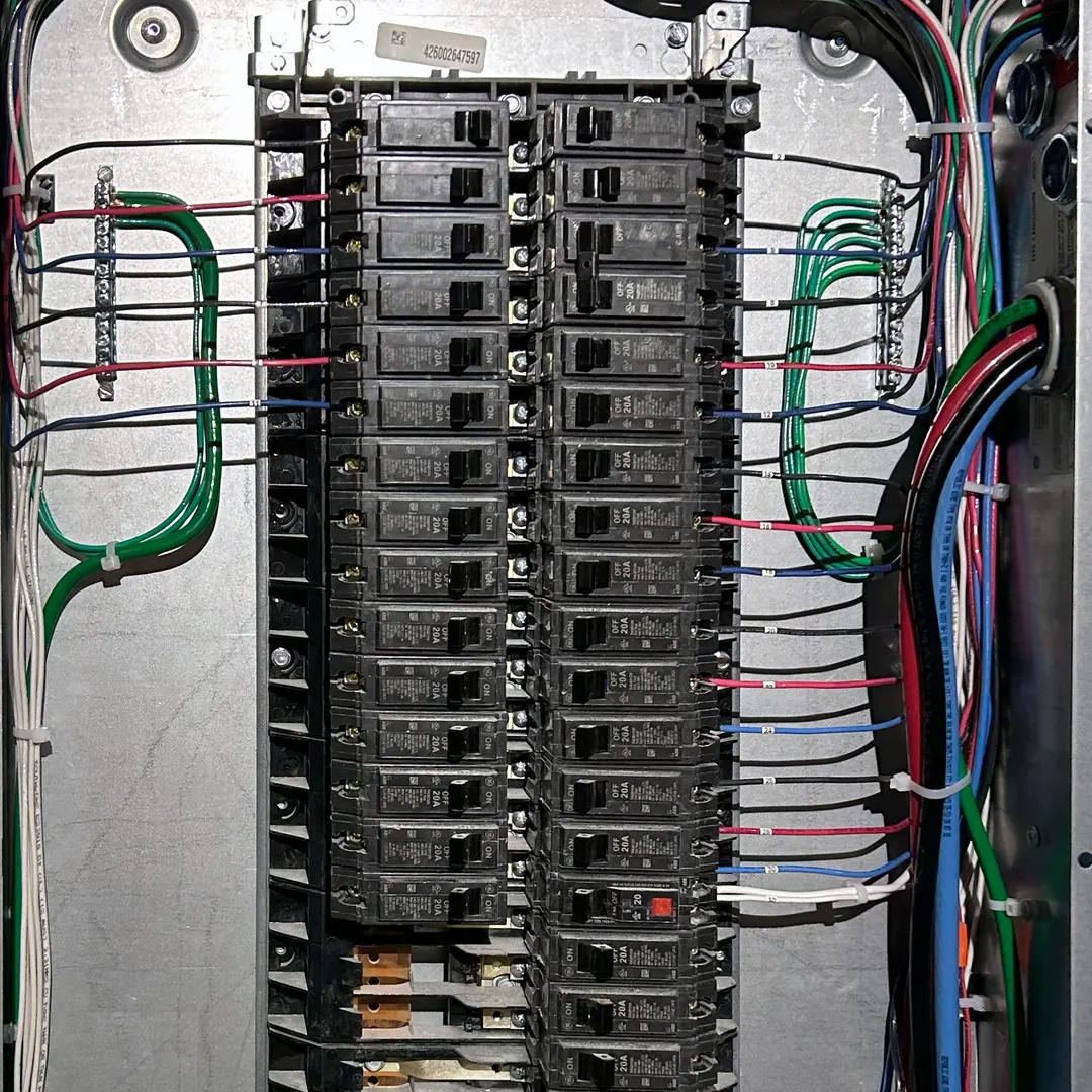 An open breaker panel set in drywall, two columns of breakers with black, red and blue circuit wires landed neatly on each side